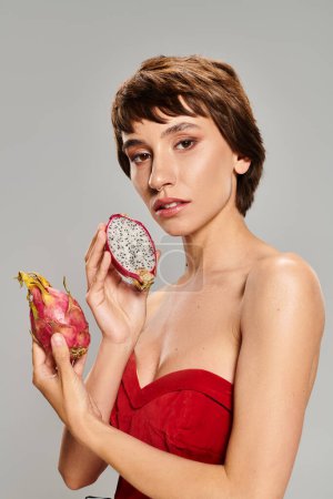 Eine junge Frau in einem roten Kleid hält eine Drachenfrucht, umgeben von leuchtenden tropischen Früchten.