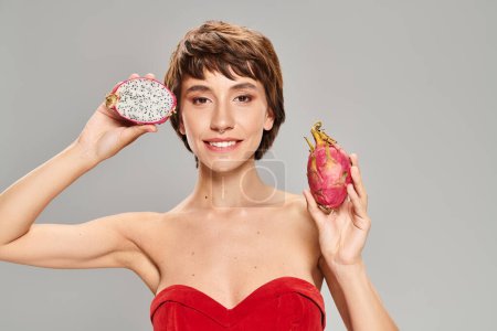 Young woman in red dress gracefully holds fresh dragon fruit.
