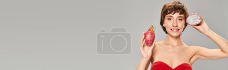 Foto de Una mujer joven con estilo en un vestido rojo sosteniendo una fruta de dragón. - Imagen libre de derechos
