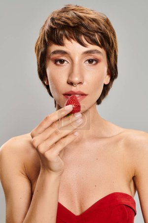 Foto de Mujer joven vestida de rojo comiendo delicadamente una fresa. - Imagen libre de derechos