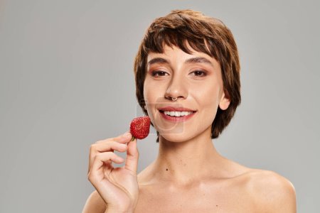 A young woman delicately holding a strawberry in her hand.