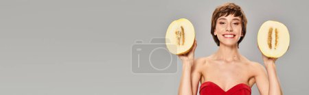 Photo for Young woman wearing a vibrant red dress, holding two pieces of fruit. - Royalty Free Image