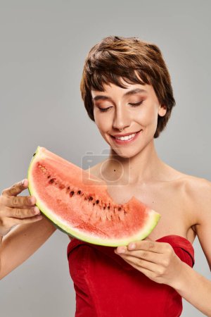 Photo for A young woman in a striking red dress holds a slice of watermelon. - Royalty Free Image