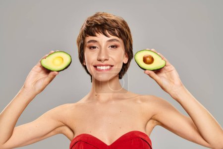 A young woman gracefully holds two halves of an avocado.