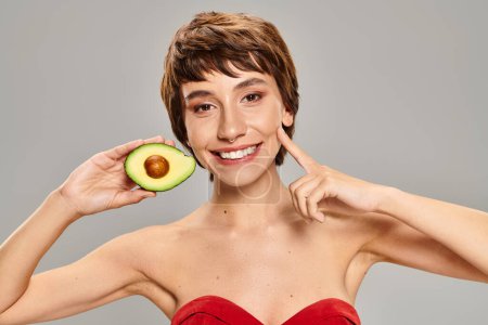 Eine Frau versteckt ihr Gesicht spielerisch hinter einer frischen Avocado.