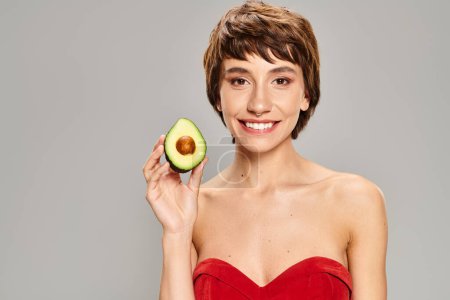 Photo for A stylish woman in a red dress holding an avocado. - Royalty Free Image