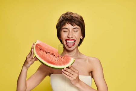 Téléchargez les photos : Jeune femme tenant une tranche de pastèque sur son visage, appréciant les couleurs vives et les fruits frais. - en image libre de droit