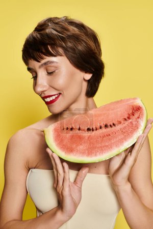 Photo for A young woman playfully holds a slice of watermelon in front of her face against a vibrant backdrop. - Royalty Free Image