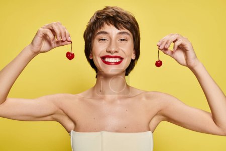 Photo for Young woman striking a pose with a cherry balanced on her head against a vibrant backdrop. - Royalty Free Image