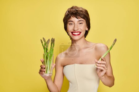Photo for A stylish young woman in a white dress holding a bunch of fresh asparagus. - Royalty Free Image