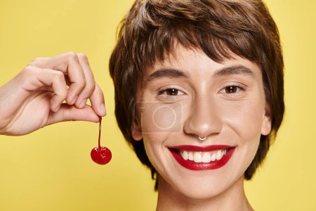 Photo for Woman holding a cherry close to her face on a colorful backdrop. - Royalty Free Image