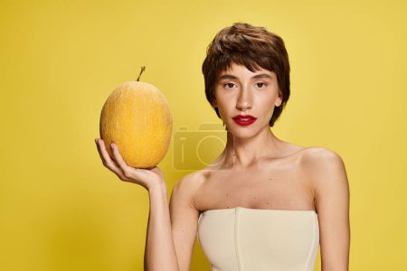 Mujer joven con un vestido blanco sosteniendo una fruta amarilla sobre un vibrante telón de fondo.