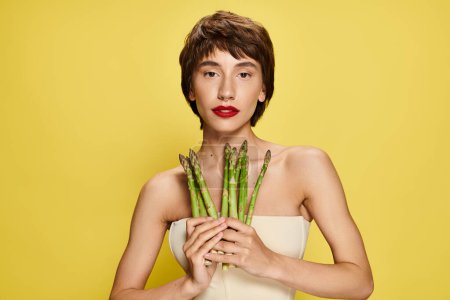 A young woman holding a bunch of asparagus in front of her face.