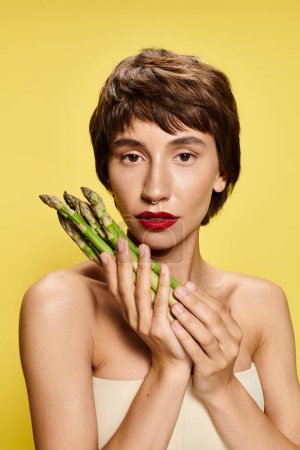 A woman playfully hides her face with a bunch of fresh asparagus.
