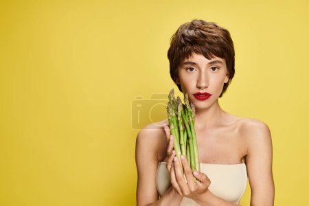 A woman playfully hides her face behind a bundle of fresh asparagus.