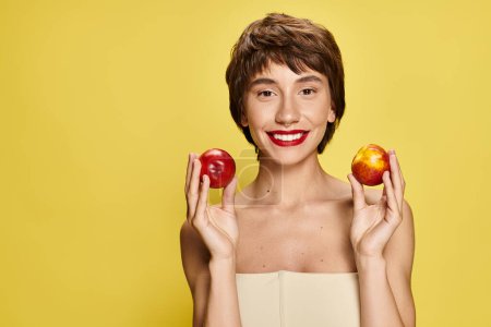 Photo for A young woman holds two peaches with one in front of her face. - Royalty Free Image