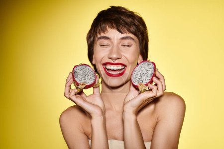 A woman playfully holds two dragon fruits in front of her face.