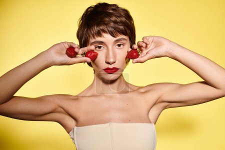 Photo for A young woman holds two strawberries in front of her face. - Royalty Free Image