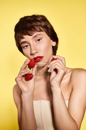 A young woman playfully holds a strawberry in front of her face.