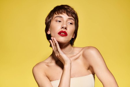 A fashionable young woman with red lipstick on her face poses elegantly on a vibrant backdrop.