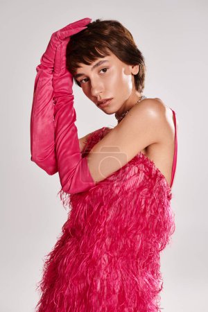 Fashionable young woman striking pose in vibrant pink feather dress.