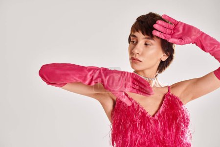 A fashionable young woman in a pink dress and matching gloves poses elegantly against a vibrant backdrop.