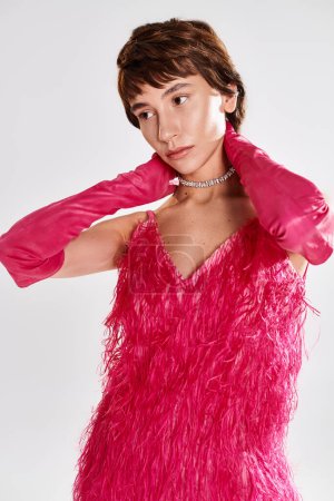 Eine modische junge Frau in einem eleganten rosafarbenen Federkleid posiert vor einer lebendigen Kulisse.