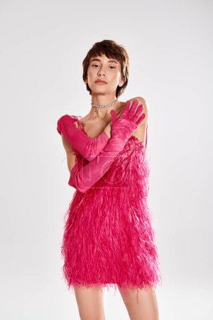Téléchargez les photos : Femme à la mode frappe une pose en robe rose et gants sur fond vibrant. - en image libre de droit