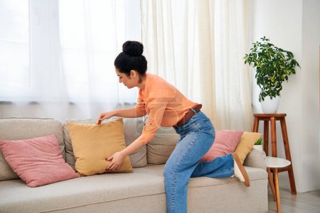 Una mujer con estilo en ropa casual se sienta con gracia en un sofá, agarrando una almohada acogedora.