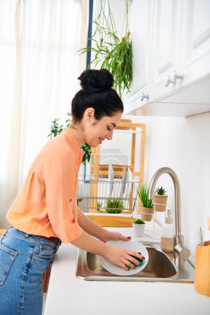 Une femme élégante en tenue décontractée lave diligemment la vaisselle dans un évier lumineux, mettant en valeur la beauté dans les tâches de routine.