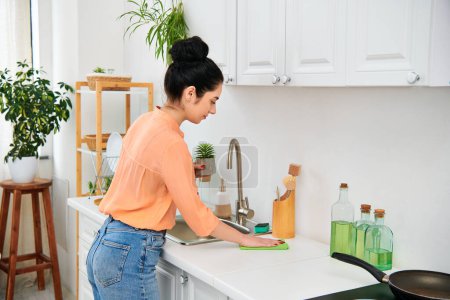 Una mujer vestida de manera casual está en un fregadero de la cocina, con una sartén en el mostrador. Ella aparece enfocada y serena mientras realiza sus tareas domésticas..