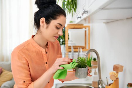 A stylish woman holding a potted plant in a cozy kitchen setting.