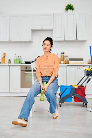 A stylish woman in casual attire sits on a chair, sparkling clean kitchen in the background.