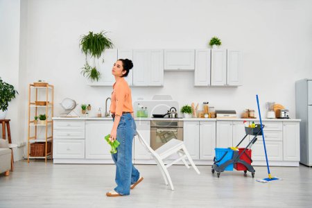 A stylish woman in casual clothes stands in a kitchen, confidently holding a mop.