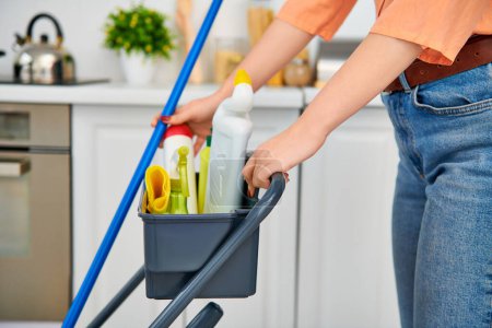 A stylish woman in casual attire gracefully cleans the floor with a mop in her home.