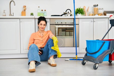 A stylish woman in casual attire sits on the kitchen floor, engaged in cleaning tasks with a calm demeanor.