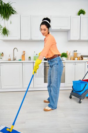 Una mujer elegante con ropa casual limpia elegantemente el piso de la cocina con una fregona, exudando elegancia y funcionalidad.