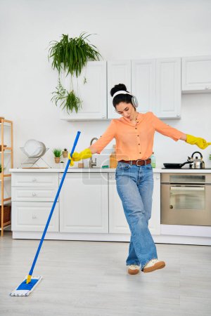 Una mujer elegante con atuendo casual limpia elegantemente el suelo con una fregona en su casa.
