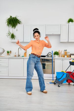 A stylish woman joyfully dances in the kitchen, wearing headphones while cleaning her home.