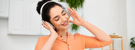 Foto de Una mujer con estilo en una camisa naranja disfruta de la música a través de auriculares. - Imagen libre de derechos
