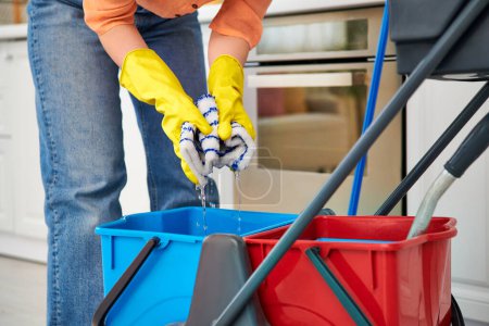 A stylish woman in casual wear gracefully mops the floor with a bucket, ensuring a clean and tidy home environment.