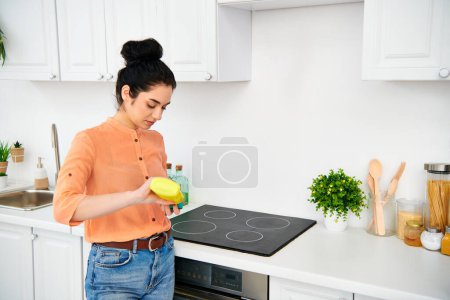Téléchargez les photos : Une femme élégante en tenue décontractée debout dans une cuisine, tenant un frisbee jaune vif. - en image libre de droit