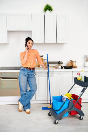 Una mujer elegante con atuendo casual de pie en una cocina hablando por un teléfono celular.