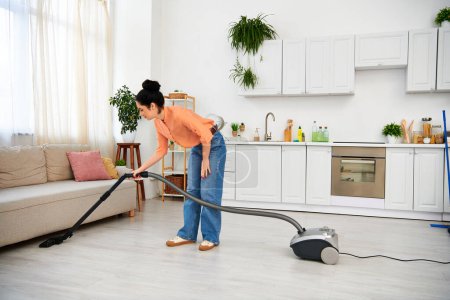 A stylish woman in casual attire efficiently vacuums a living room, leaving it spotless and fresh.
