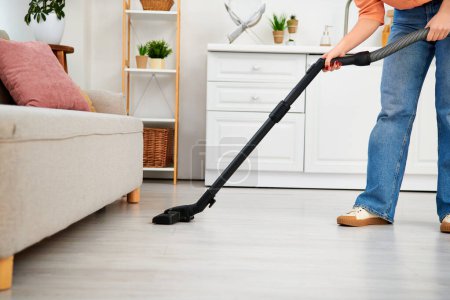 Photo for A stylish woman in casual attire using a vacuum cleaner to tidy the floor of her home. - Royalty Free Image
