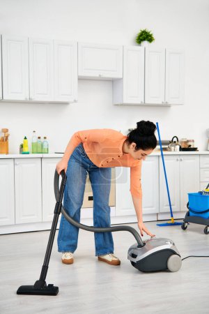 A stylish woman in casual attire passionately cleans her kitchen floor using a vacuum cleaner.