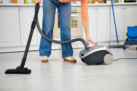 A stylish woman in casual attire gracefully vacuums the kitchen floor.