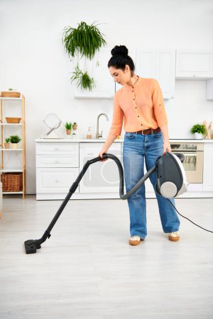 A stylish woman in casual attire efficiently vacuums her kitchen floor to keep her home spotless.