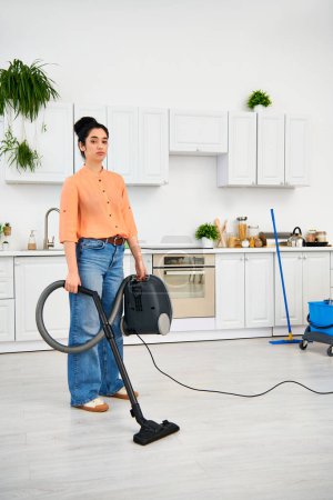 A stylish woman in casual attire gracefully vacuums the kitchen floor to keep it clean and tidy.