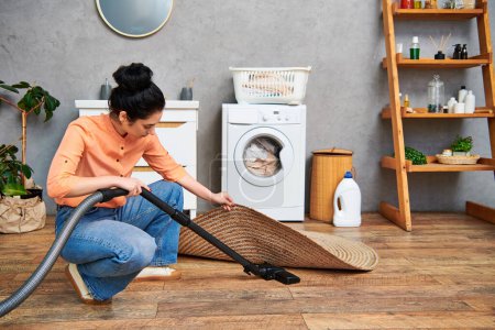A stylish woman in casual attire cleans the floor with a vacuum cleaner in a home setting.